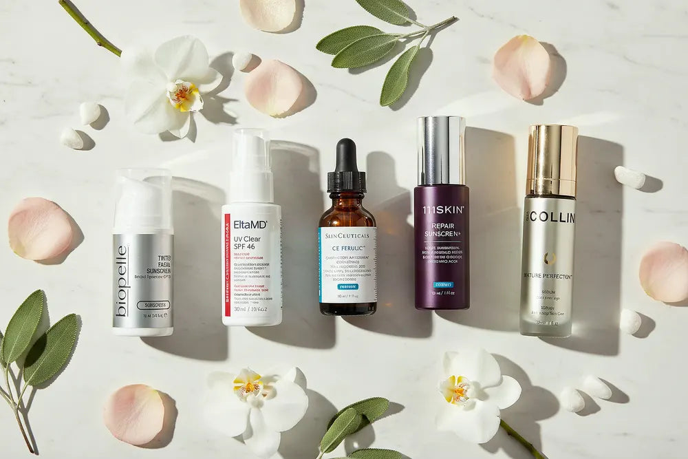 Professional skincare from the Le Petit Skincare edit, laid out on white marble with orchids, rose petals and sage